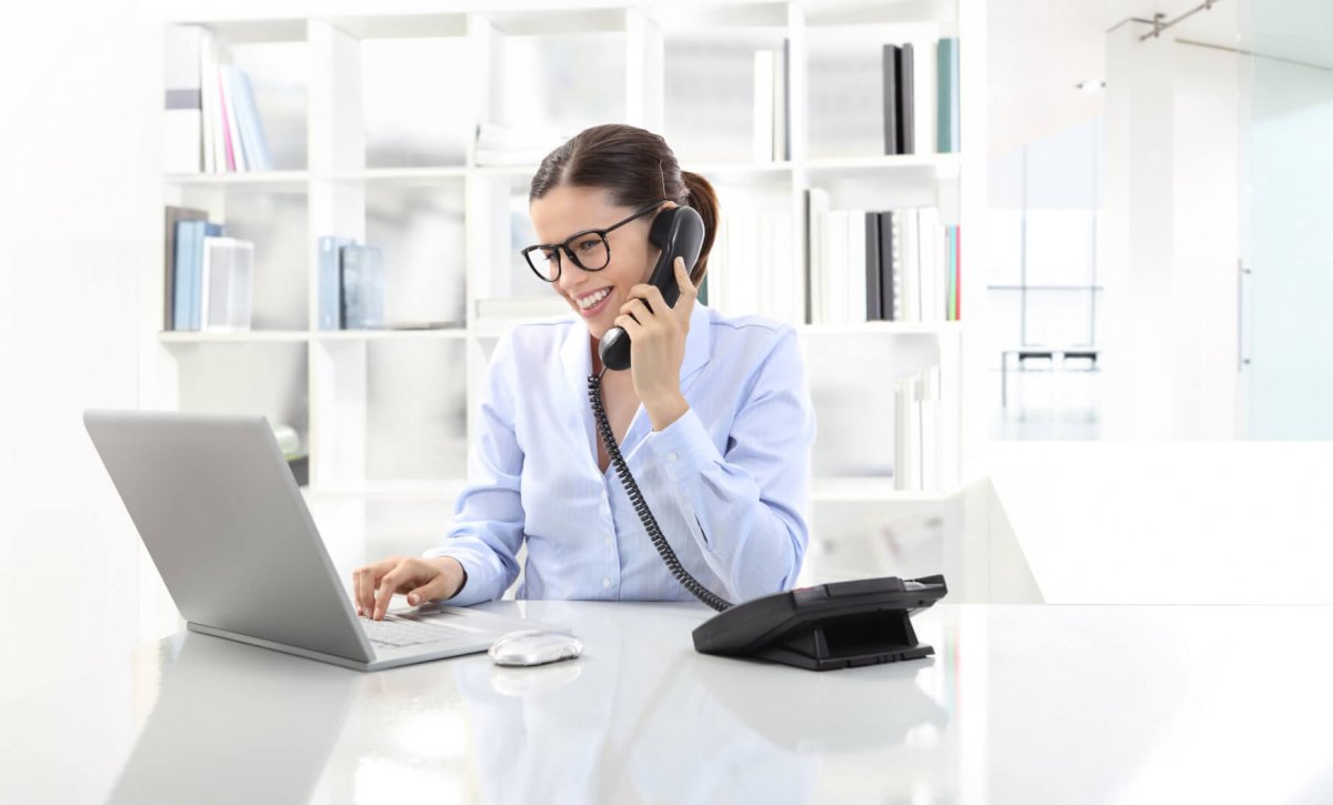 smiling woman in office at desk with computer, talking on the phone
